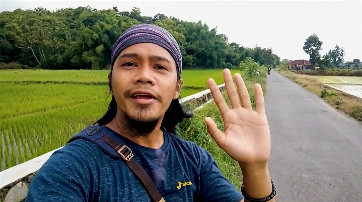 A local guide waving from a rural road beside green rice paddies in Yogyakarta, Indonesia